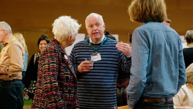 Drie mensen staan in een zaal en praten met elkaar