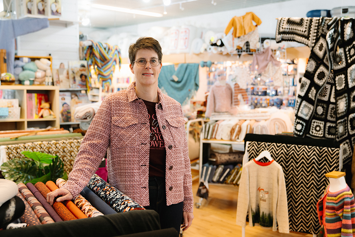 Vrouw staat in een winkel met stoffen en handwerkmaterialen.