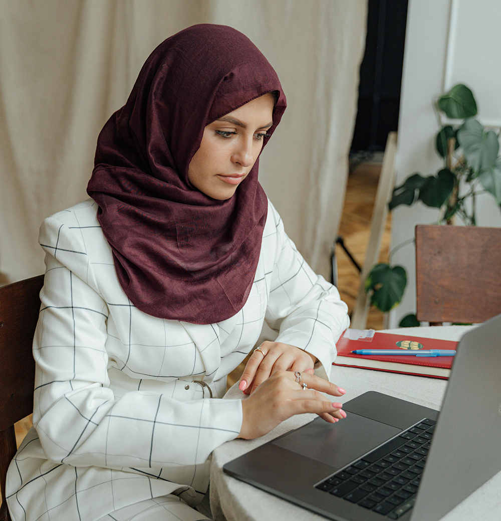 Vrouw zit aan tafel en werkt op een laptop.