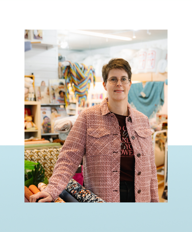 Vrouw staat in een winkel met stoffen en handwerkmaterialen.