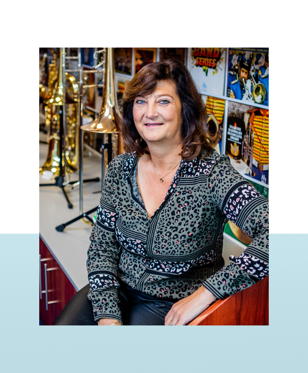 Vrouw zit op een toonbank in een muziekwinkel met blaasinstrumenten op de achtergrond.