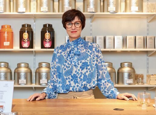 Vrouw staat achter een toonbank in een winkel met potten en verpakkingen in het schap.