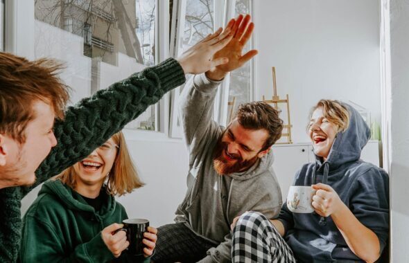 Vier personen zitten bij elkaar in een woonkamer en geven elkaar een high five.