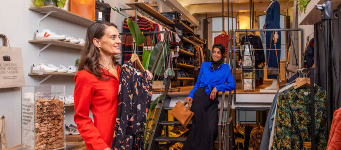 Twee vrouwen in een kledingwinkel, één toont een jurk aan de ander.