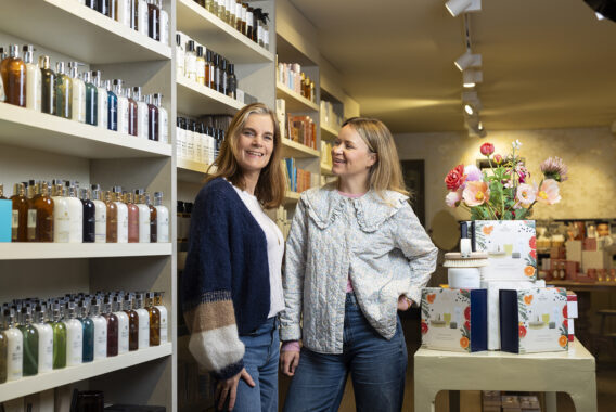 Twee vrouwen staan lachend tussen schappen met parfums en verzorgingsproducten.