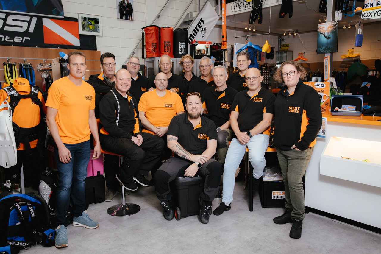 Groep medewerkers poseert samen in een duikwinkel.
