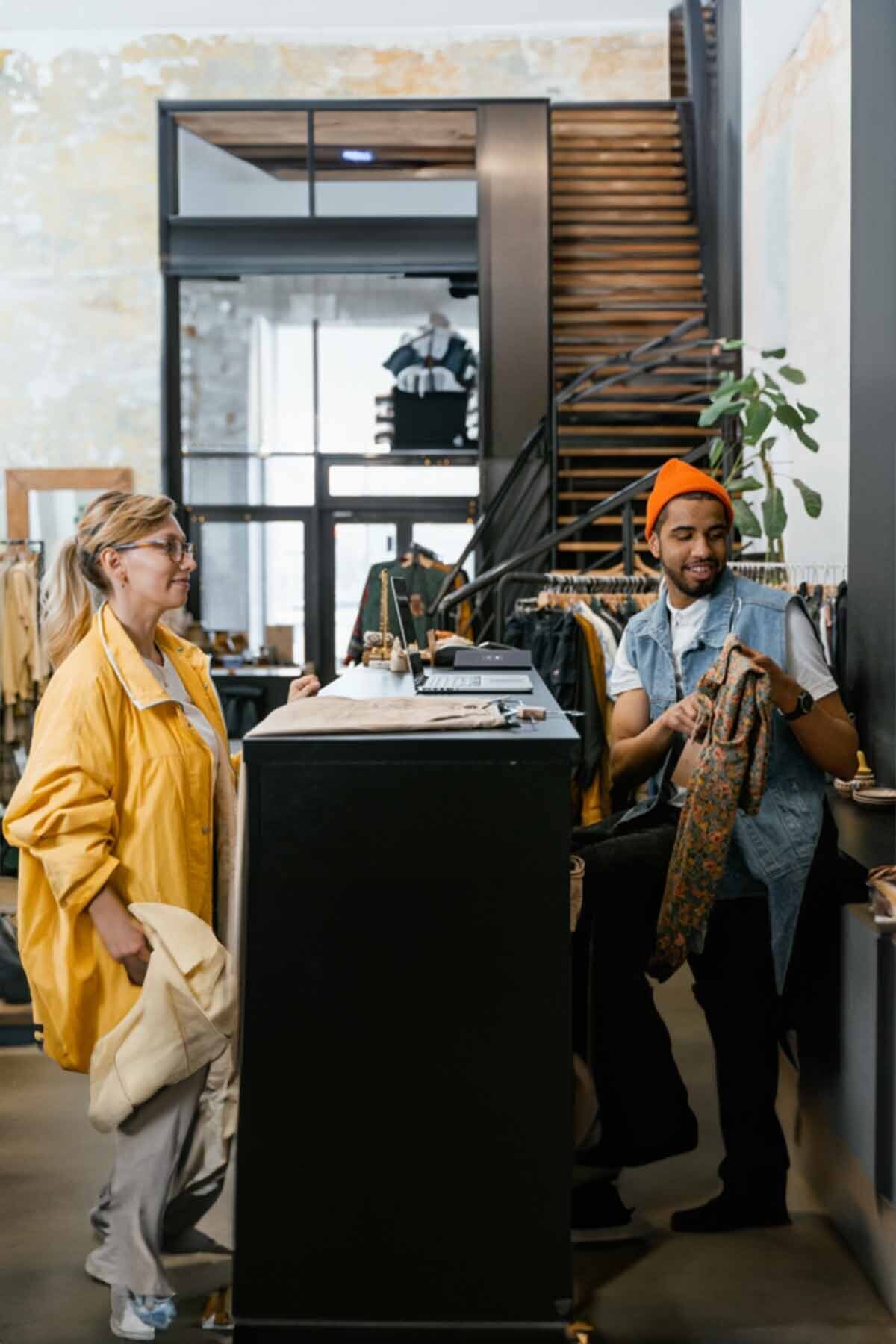 Vrouw staat bij een toonbank terwijl een man een kledingstuk vasthoudt in een winkel.