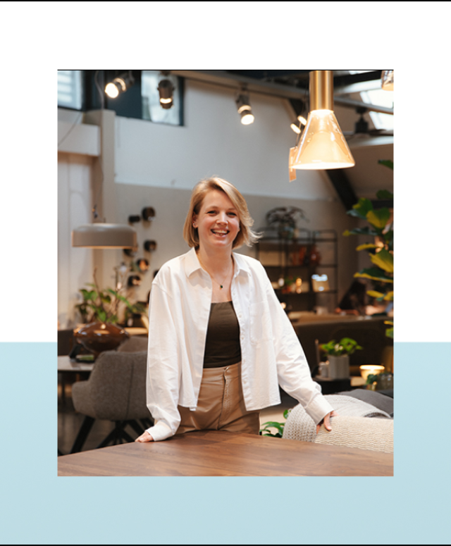 Vrouw staat lachend achter een houten toonbank in een winkel met planten op de achtergrond.