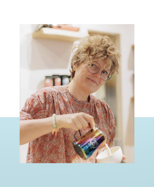 Vrouw met bril en krullend haar schenkt iets uit een kleurrijk pak in een kopje in een winkel.