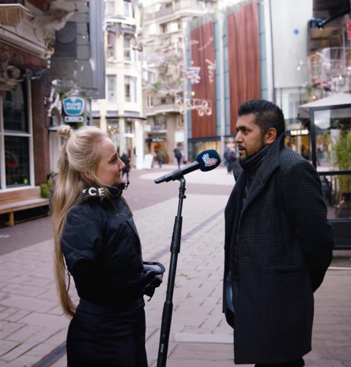 Twee personen staan tegenover elkaar op straat met een microfoon tussen hen.