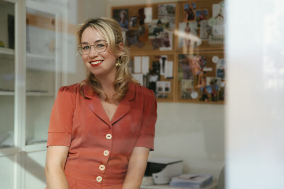 Vrouw zit in een kantoorruimte met een prikbord op de achtergrond.