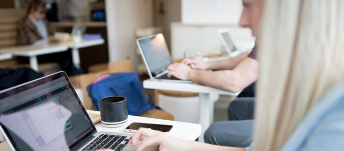 Personen zitten aan tafels en werken op laptops in een ruimte.