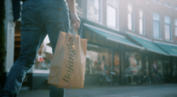 Persoon loopt door een winkelstraat en draagt een papieren winkeltas.