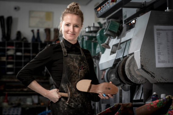Vrouw staat in een werkplaats en houdt een schoenzool vast.