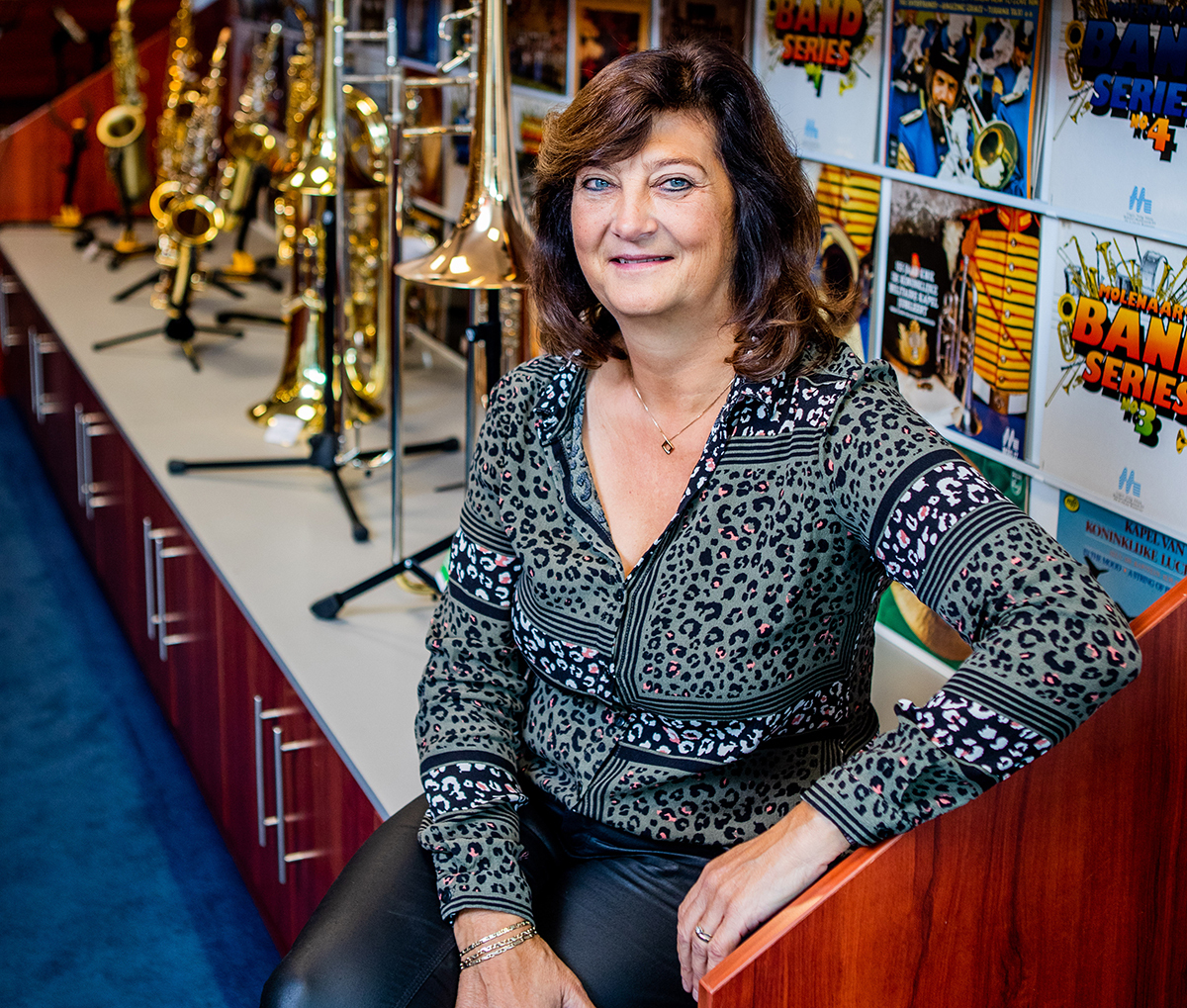 Vrouw zit op een toonbank in een muziekwinkel met blaasinstrumenten op de achtergrond.