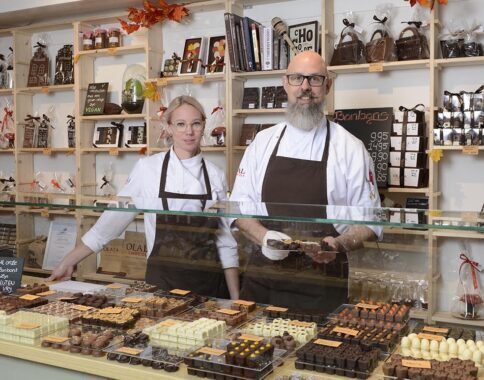 Twee medewerkers staan achter een toonbank met chocolade in een winkel.